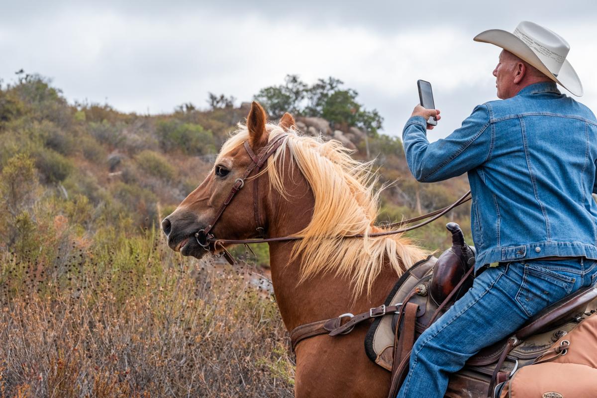 A rider on a hillside trail holds up his phone from the saddle, the moment the does GPS work off grid trails question matters